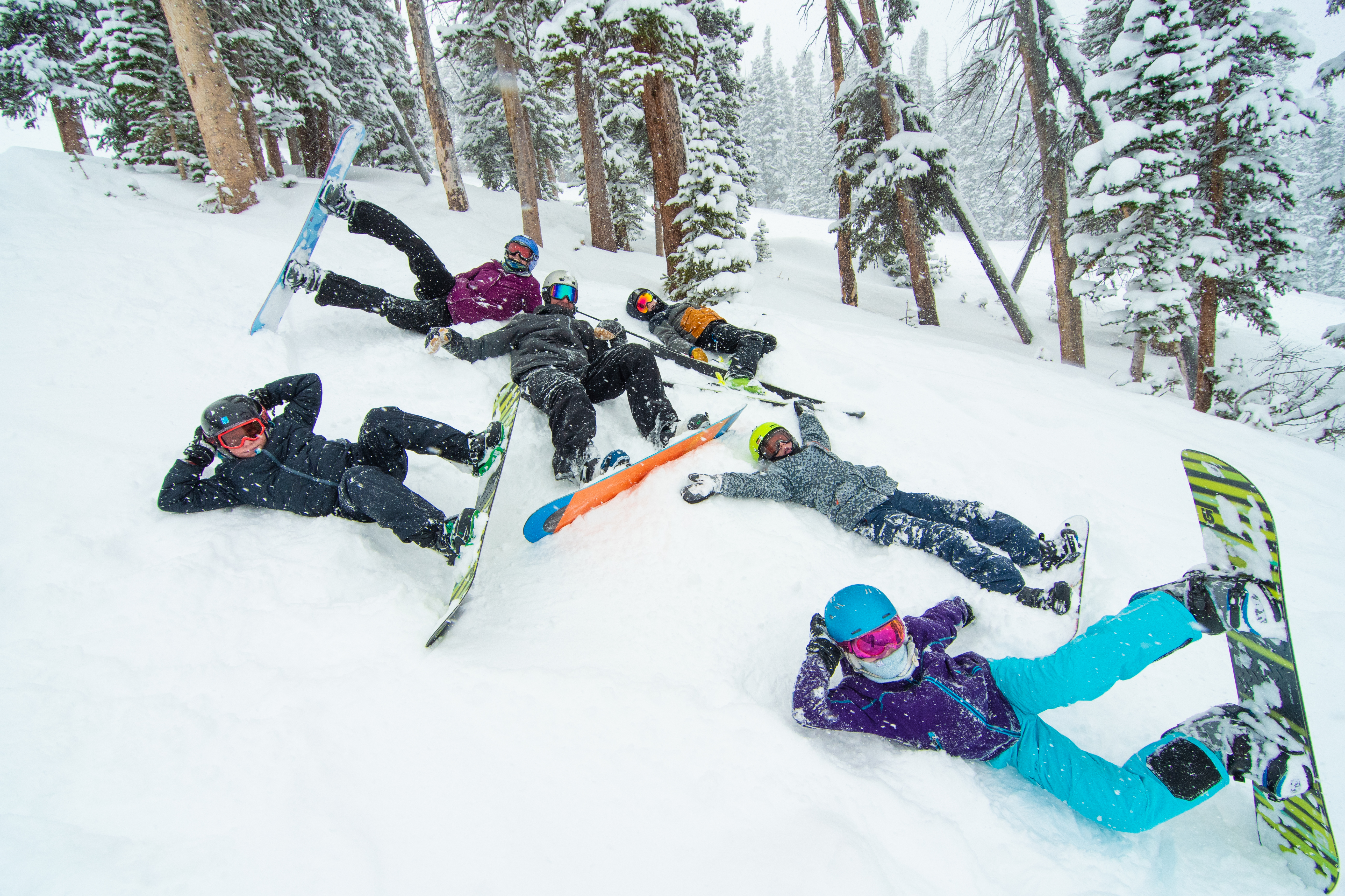 a group of kids poses while lying on the ground in the snow with snowboards strapped to their feet